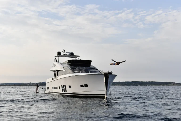 Luxury yacht on calm waters with a person diving off the bow and another paddleboarding nearby, showcasing a premium concierge yacht charter experience.